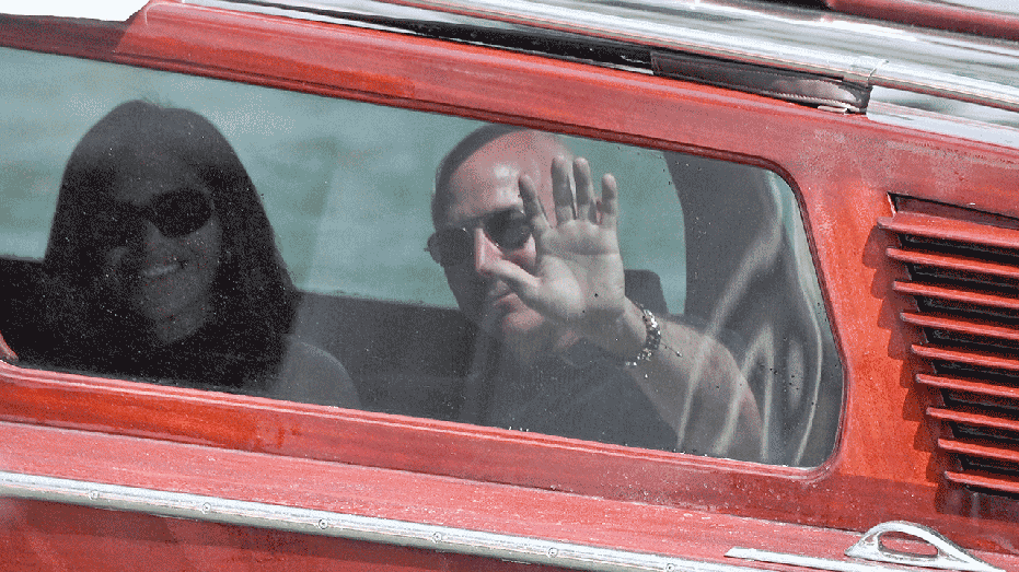 Amazon's founder Jeff Bezos waves and Lauren Sanchez smiles in a boat