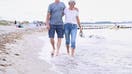A retired couple walks arm in arm on the beach.  - Fox Business News